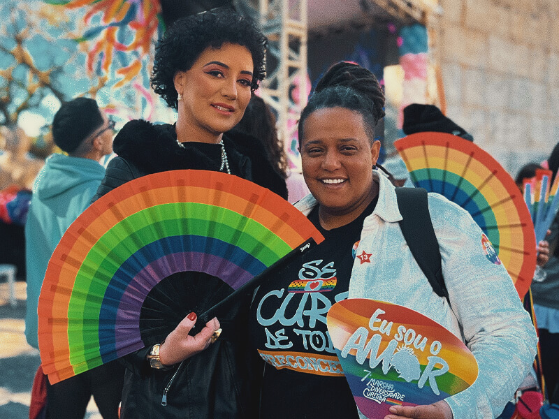 Giorgia Prates ao lado de uma mulher segurando leques coloridos